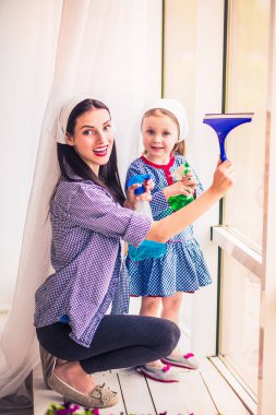 Young beautiful smiling housewife washes windows with her daughter indoors clipart