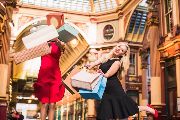 Two happy attractive women jump with shopping bags in hands, indoors