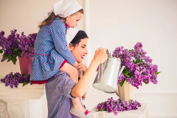 Jovem Mãe Feliz Mantém Filha Seus Ombros Rega Flores Casa — Fotografia de Stock
