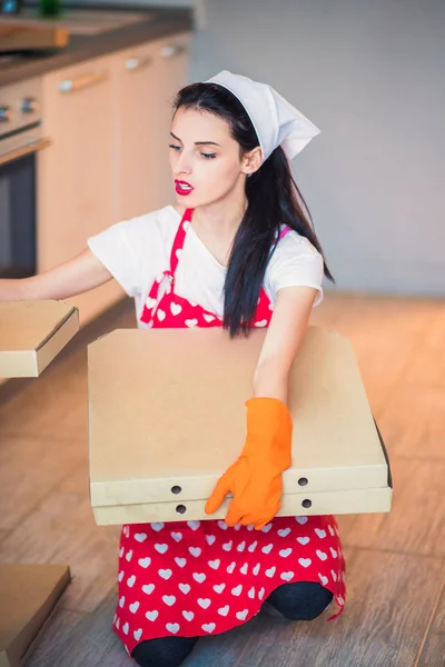 Portrait of a young weary housekeeper who sits on the floor in kitchen and keeps pizza boxes