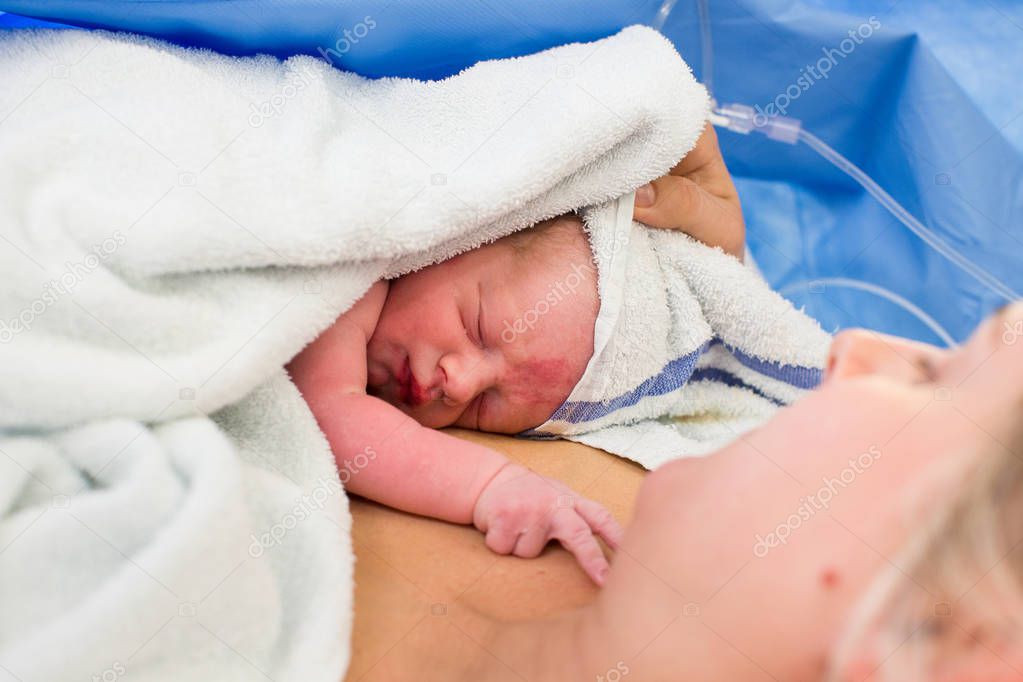 Close-up newborn baby wrapped in a towel lies on mother who looks at baby indoor