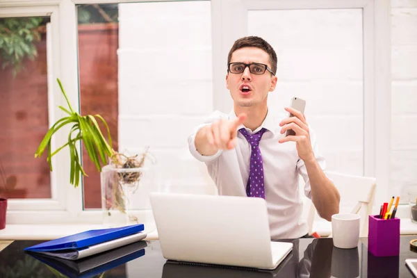 Young businessman looks forward, his forefinger shows forward and keeps the phone in hand at the office