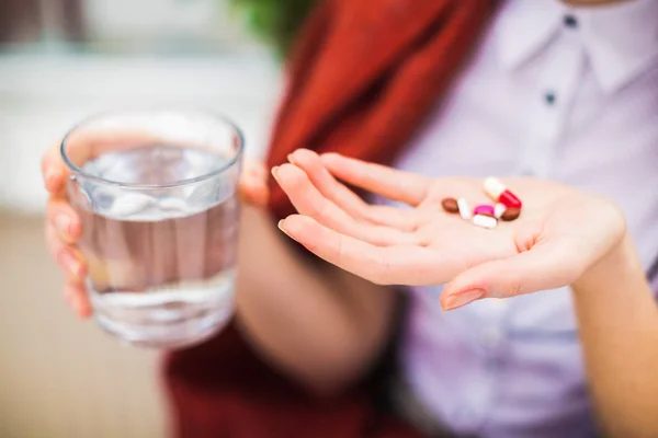 Close-up several pills in hand of sick woman and cup of water in other hand