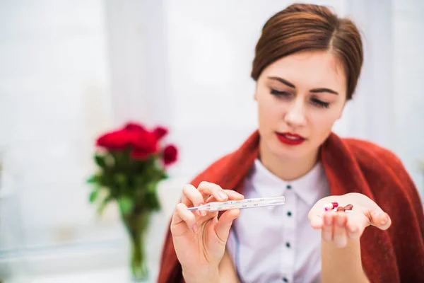 stock image Close-up photo of sick woman who keeps thermometer and several pills in hands indoor