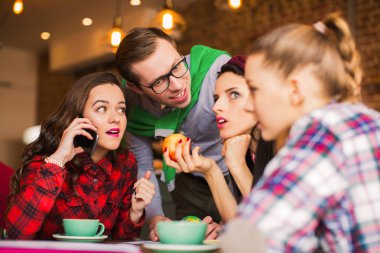 Bir grup insan kafede oturur ve onlardan biri telefonda konuşuyor, diğerleri bu konuşmada zaman ara dinle