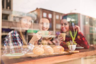 Üç güzel kadın croissants ve kahve bir kafede ellerinde ile masaya oturup