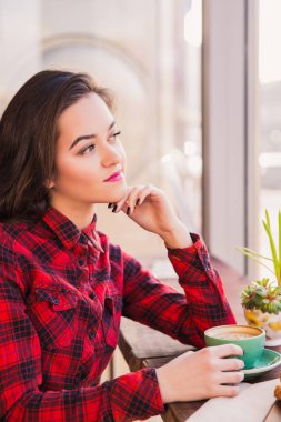Portre güzel esmer kahve pencerenin yakınındaki ile masada oturur ve pencere, kafede bakar