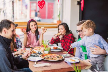 Mutlu insanların grup ile farklı yemek masada oturur, bir adam küçük bir çocuk restoranda tutar.