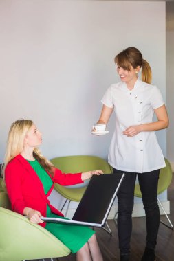 Mutlu müşteri oturur ve dergi, Ofis Yöneticisi getirdi fincan kahve stomatology klinikte istemciye, tutar