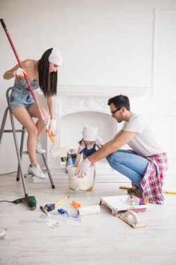 Genç aile evde tamir, gülümseyen anne merdiven üzerinde duruyor ve panel tutar, baba boya tutar, kızları onlara yardımcı olur