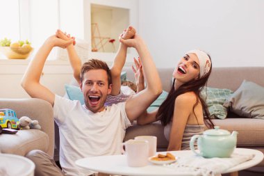 Ebeveyn odasında ve küçük oğulları kanepe ve babası onu bacaklar tarafından çekerek yatan katta masada oturan gülümseyen genç