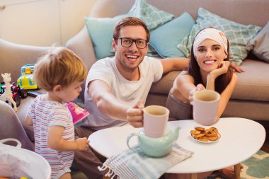 Genç gülümseyen odasındaki masada oturan ve küçük oğlu yakınındaki çay bardağı tutmak veliler oynayan