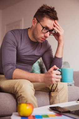 Genç yorgun adam dizüstü izliyor ve kapalı sıcak içme