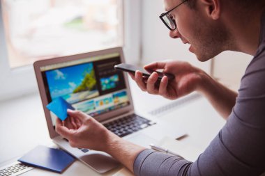 Dizüstü bilgisayar kullanarak ve kapalı telefonla konuşan genç adam