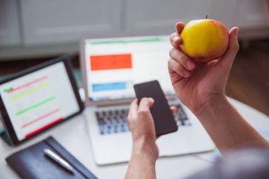 Elinde bir elma ve çalışma şeyler masada kapalı arka planı başka bir elinde telefon yakın çekim