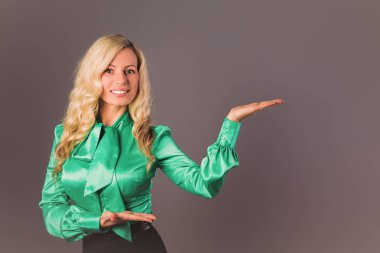 Gri arka plan üzerinde duran ve gösterilen jestleri genç zarif sarışın kadın portresi