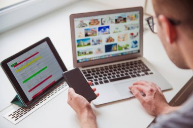 Dizüstü bilgisayar kullanarak ve telefon elinde kapalı tutarak yakın çekim Genç adam