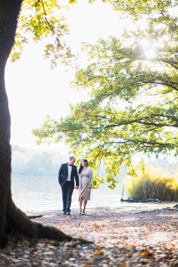 Hamile bir ilahi kadın kocasıyla gölet yakınındaki yürür ve eller birbirlerini tutuyorlar