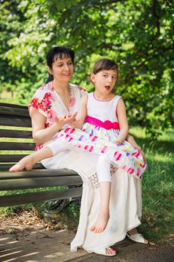 Mutlu genç bir bankta oturan ve onun ilahi kızı açık havada tur üzerinde devre dışı tutan anne