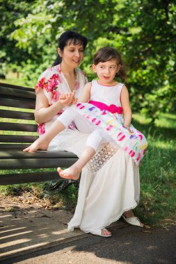 Mutlu genç bir bankta oturan ve onun ilahi kızı açık havada tur üzerinde devre dışı tutan anne