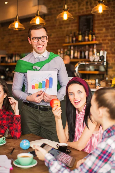 Successful man shows a paper with graph for group of people, in a cafe