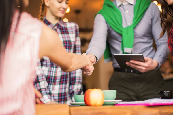 Two partners shake hands in company of people, in time of a break, in a cafe