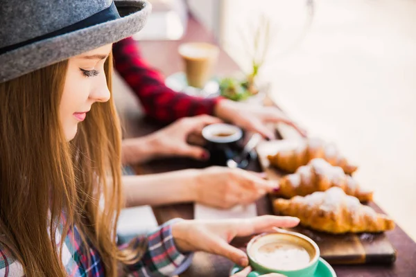 Face of beautiful woman who sits at the table with croissants and keeps cup of coffee