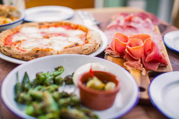 Sliced meat, the pizza and other food on the table in restaurant