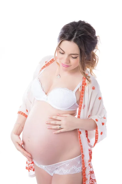 若いの穏やかな妊娠中の女性は白い背景に対して立っていると彼女の腹に手を保つし それを見る人の肖像画 — ストック写真