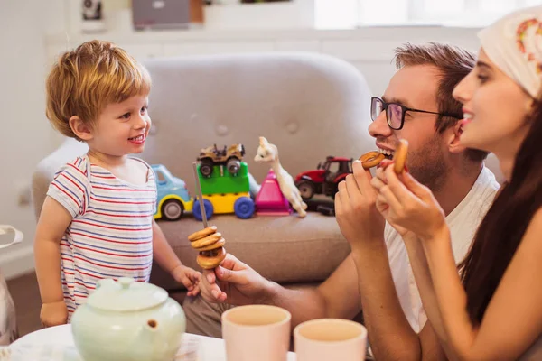 若い幸せな親部屋のテーブルに座って それらを見て幼い息子の近くのベーグルを食べること — ストック写真