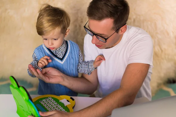年轻英俊的父亲和他可爱的小儿子在室内玩玩具笔记本电脑 — 图库照片