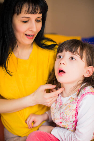 Маленькая красивая девочка-инвалид сидит на коленях своей молодой веселой матери в помещении
