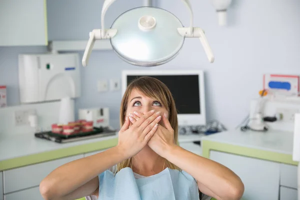 Frightened woman at dentist office covered mouth with hands.