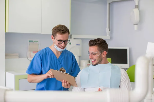 Medicine and health care concept - happy male dentist with patient talking at dental clinic office.
