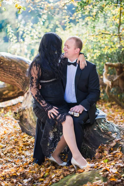 A young pregnant woman sits on lap of her happy husband who keeps little shoes in the park and they look at each other