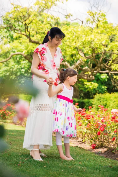 彼女の妖艶で庭を歩いて若い母娘と彼女の手と花を見て彼らを無効に — ストック写真