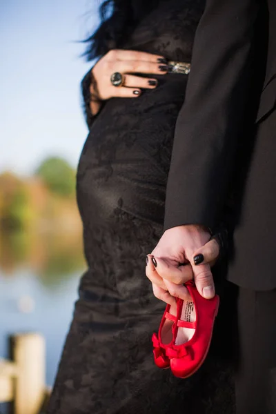 彼の妊娠中の奥さんの屋外に立って将来の父の手に小さな赤い靴を閉じる — ストック写真