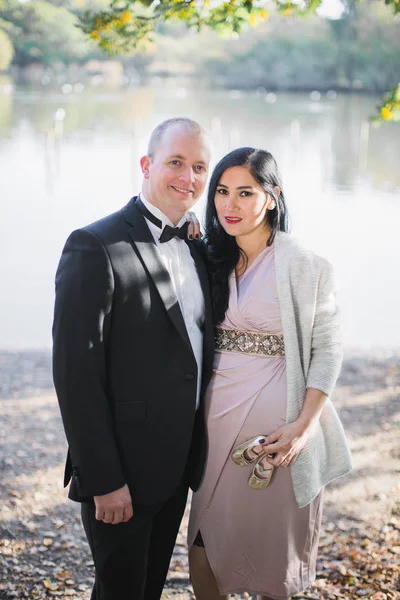 一个怀孕的温柔女人的肖像 她站在丈夫身边 手里拿着小鞋 在池塘的背景下 — 图库照片