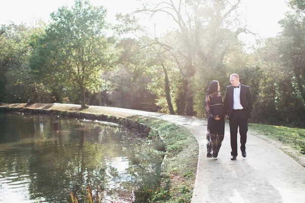 妊娠中の若い女性は幸せな夫と公園の池の近く歩くし 彼らはお互いの手を保つ — ストック写真