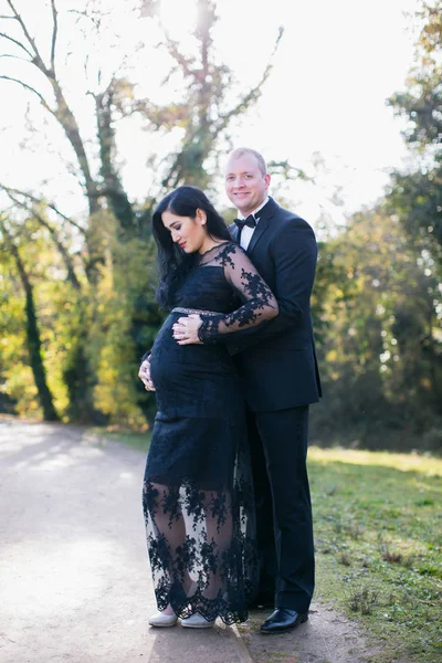 幸せ妊婦公園で夫と抱擁で立っている彼女の腹に手を保持し それを見る — ストック写真