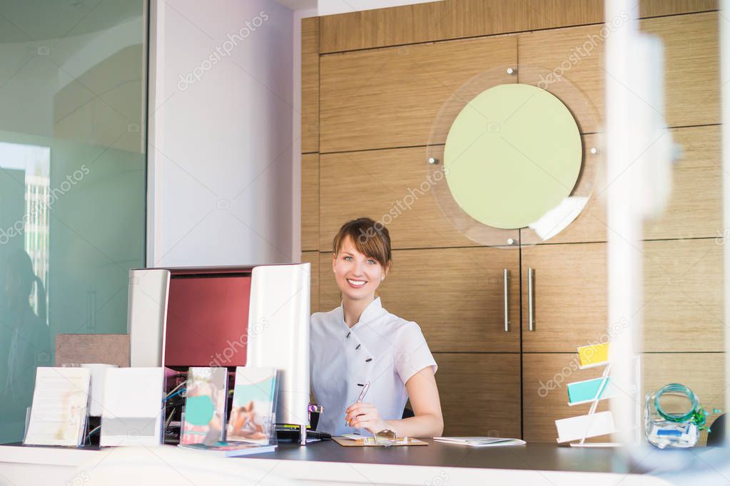 Charming smiling office-manager sits at the reception of stomatology clinic
