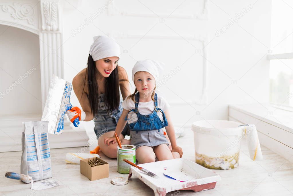 The young charming mother sits on laminate with her cute daughter and they do repair at home