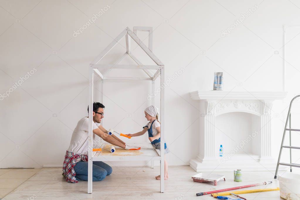 Side view of young happy father with his little daughter who do repair at home, happy daughter paints arms of father with help of platen