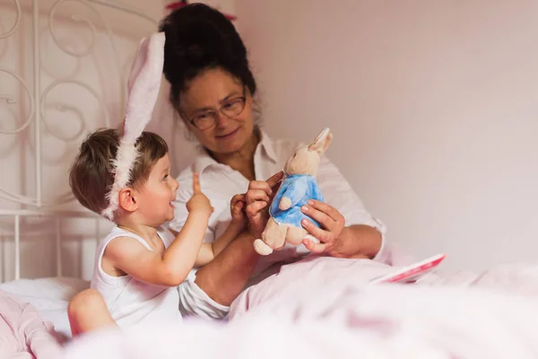 Щаслива Бабуся Усміхнений Маленький Онук Вухах Кролика Сидять Ліжку Кімнаті — стокове фото