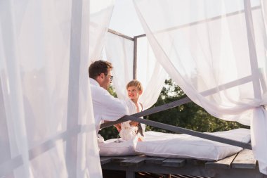 Sevimli küçük oğlu ile açık bir yatak üzerinde oturan mutlu genç baba