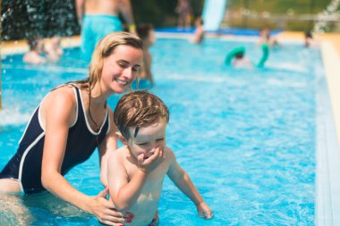 Güzel genç anne küçük oğlu bir havuzda yüzmek için öğretim