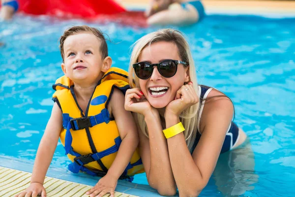 The smiling beautiful young mother in a pool with her cute little son outdoor