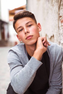 Yolda eski evin duvarının yakınında oturan yakışıklı genç adam portresi