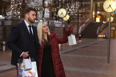 Alışveriş torbaları ile sokakta duran ve dükkanda seyir mutlu, zarif genç çift yan görünüm