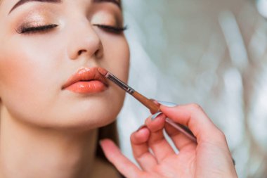 Güzel genç kadın için kapalı dudak parlatıcısı uygulayarak makyaj sanatçısı kapatın